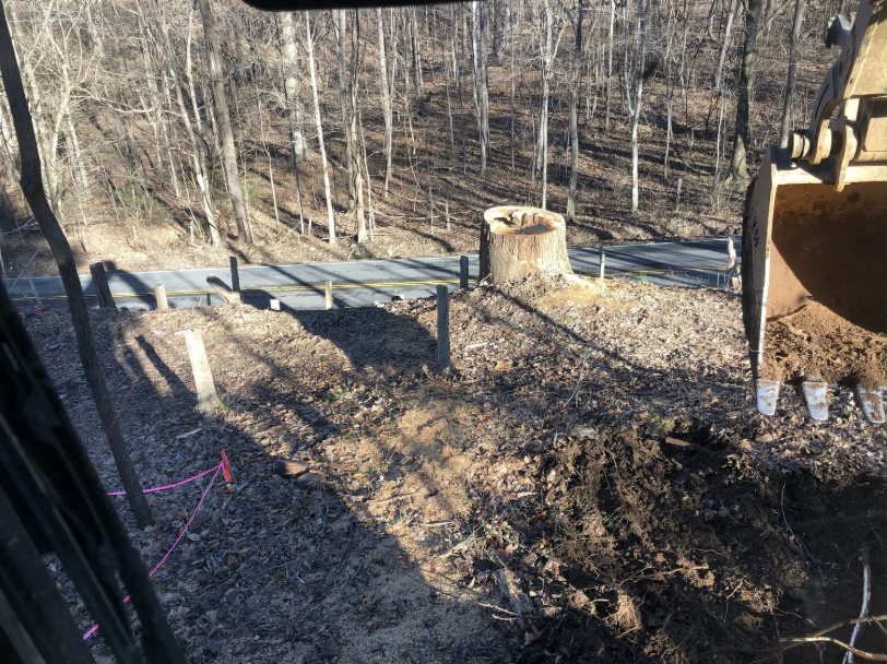 KG Excavating land clearing project — tree stump removal along a driveway cut in a wooded lot